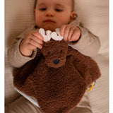 A baby lying on a bed, holding a brown plush security blanket shaped like a moose with white antlers.