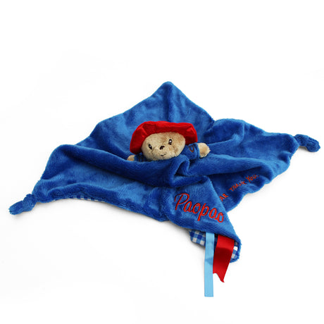 A blue soft Paddington baby soother, with a name embroidered in red and a small red and blue ribbon.