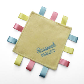 A personalised baby taggy comforter with soft yellow fleece front, embroidered with the name and date of birth