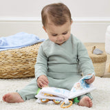 Baby sitting on a cream rug exploring the Peter Rabbit fold out activity book, with sensory tabs and crinkle pages