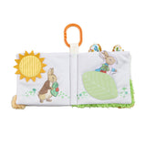 Peter Rabbit fold out activity book open showing Mr McGregor and Peter Rabbit pages with yellow sun teether, green leaf crinkle panel and textured grass edge