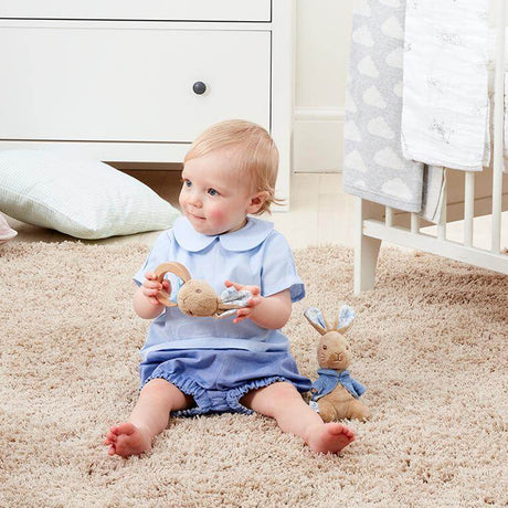 Baby in a blue outfit playing with toys on a carpeted floor.