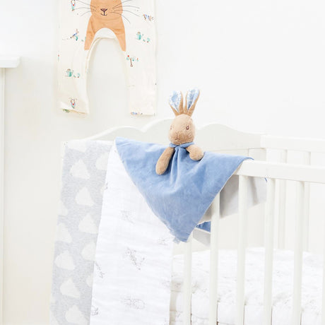 Baby crib with a blue Peter Rabbit  security blanket and plush toy in a nursery setting