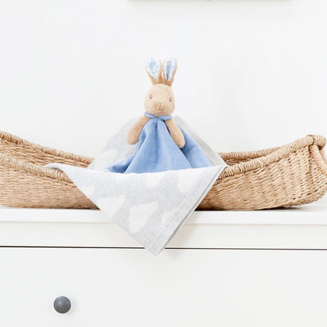 Plush toy with a blue blanket in a woven basket on a white surface