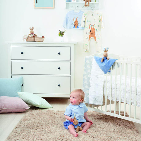 Baby in a nursery with a white dresser, crib and peter rabbit toys