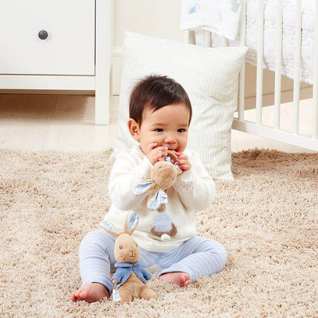 Baby sitting on a carpeted floor with toys in a nursery setting