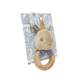 Plush rabbit toy with wooden ring and 'Peter Rabbit' text on a blue patterned background