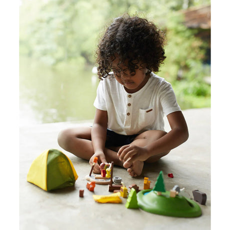 Child playing with toy camping set on a light surface with a blurred natural background