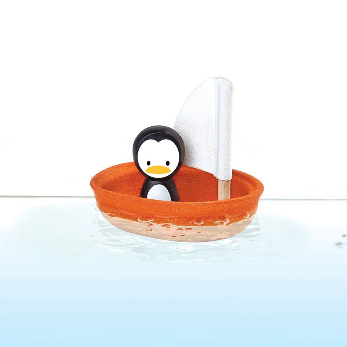 Toy penguin in an orange boat with a white sail on a white background