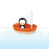Toy penguin in an orange boat with a white sail on a white background