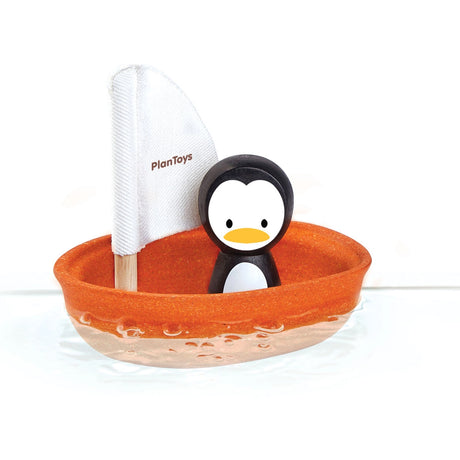 Toy penguin in an orange boat with a white sail, branded 'PlanToys', on a white background.
