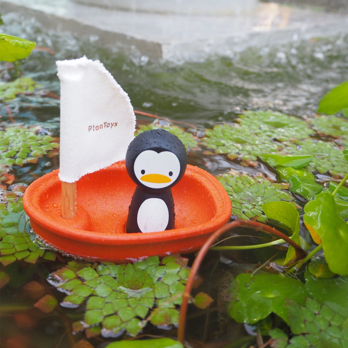 Penguin toy with a sailboat on a pond