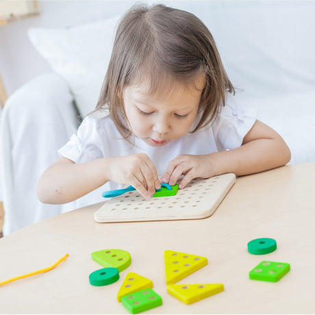 child playing with wooden lacing board with green and yellow shapes