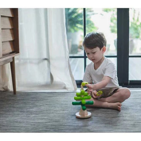 Little boy playing with green wooden Stacking tree toy with a natural wood base on a white background