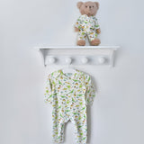 Children's bodysuit with dinosaur pattern under a white shelf with teddy on against a light gray wall.