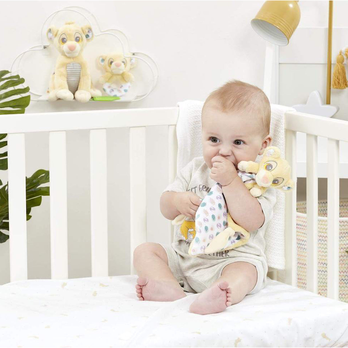 Baby sitting in a crib with lion king soother  in a nursery setting