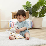 Child playing with a plush dumbo toy on a rug in a room with plants and baskets.