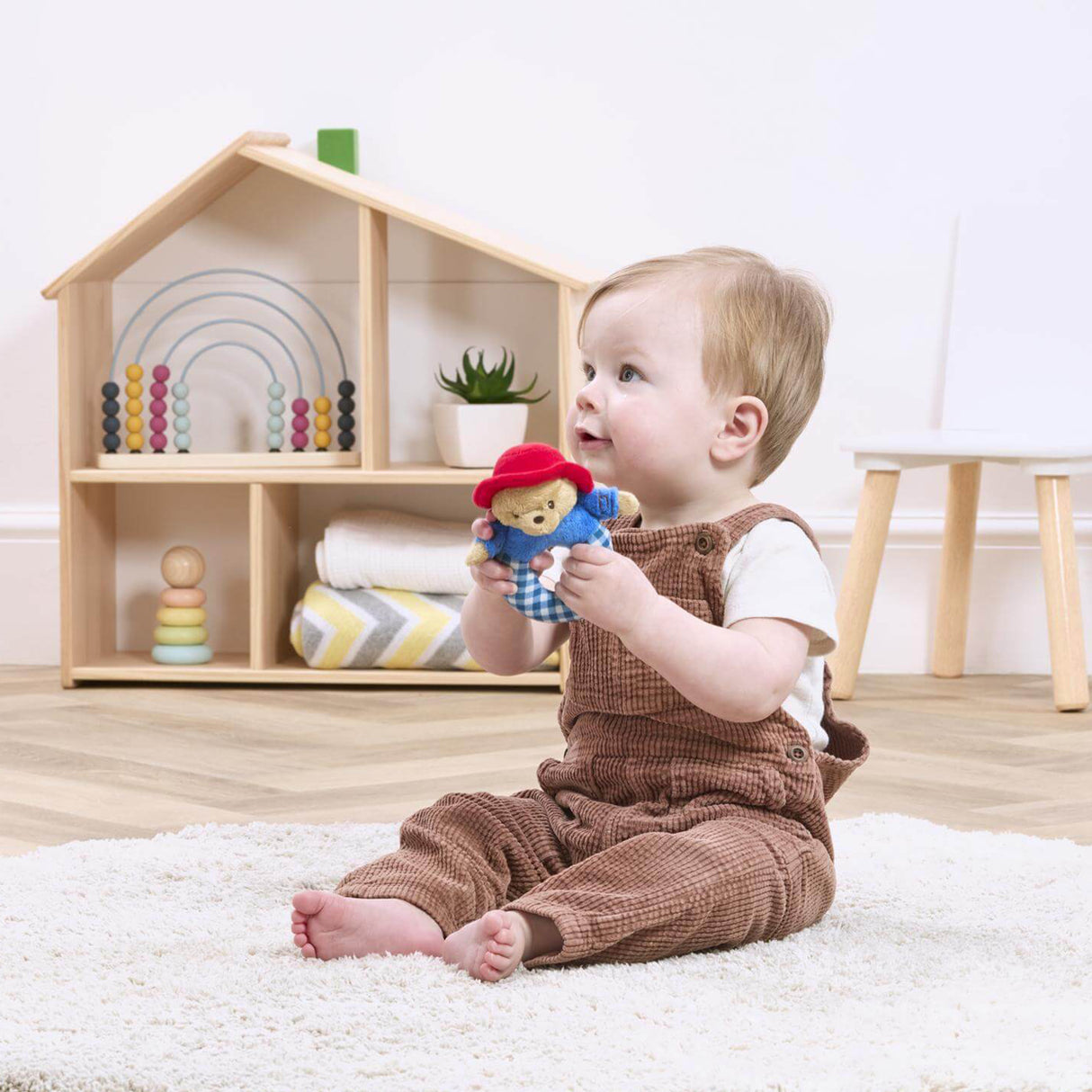 Baby playing with a Paddington toy in a room with a wooden shelf and toys.