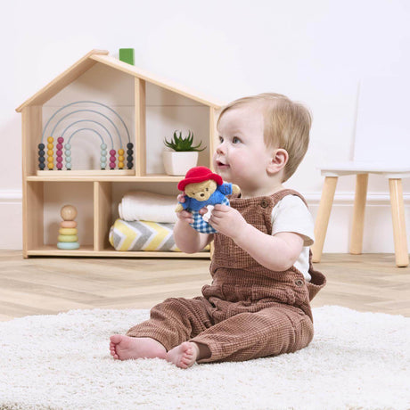 Baby playing with a Paddington toy in a room with a wooden shelf and toys.