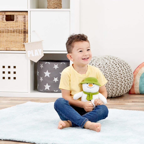 Child sitting on a bed holding a plush snowman toy in a room with storage bins and a colorful pillow.