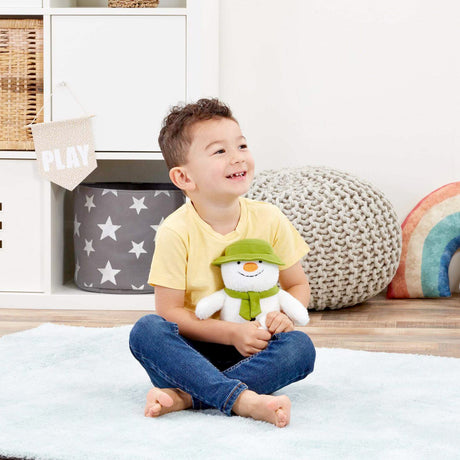 Child sitting on a bed holding a plush snowman toy in a room with decorative pillows and storage bins.