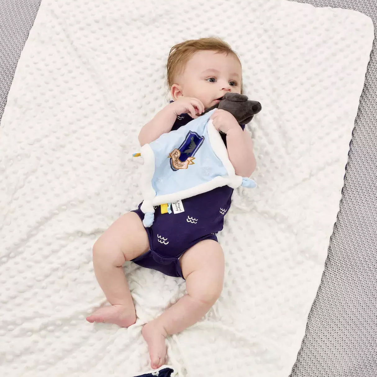 Baby lying on a harry potter Ravenclaw soother comfort blanket wearing a navy blue bodysuit