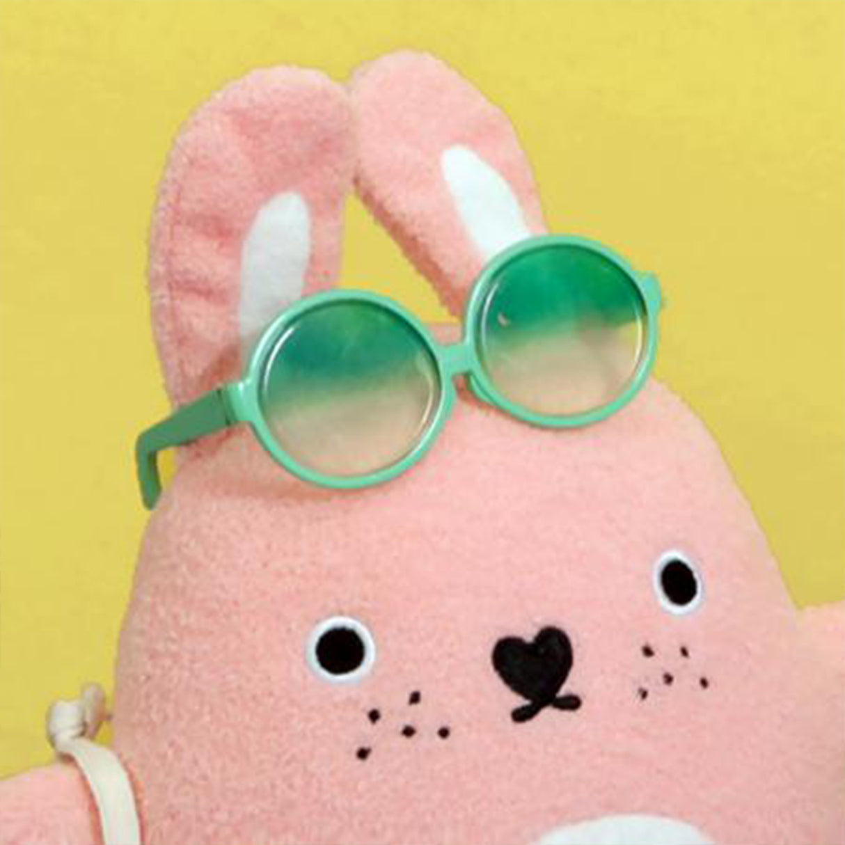 Pink plush rabbit toy with green sunglasses on a yellow background