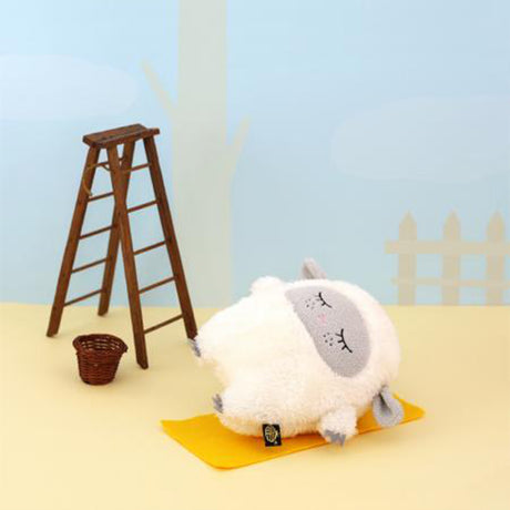 Plush toy sheep on a yellow mat with a wooden ladder and basket in the background