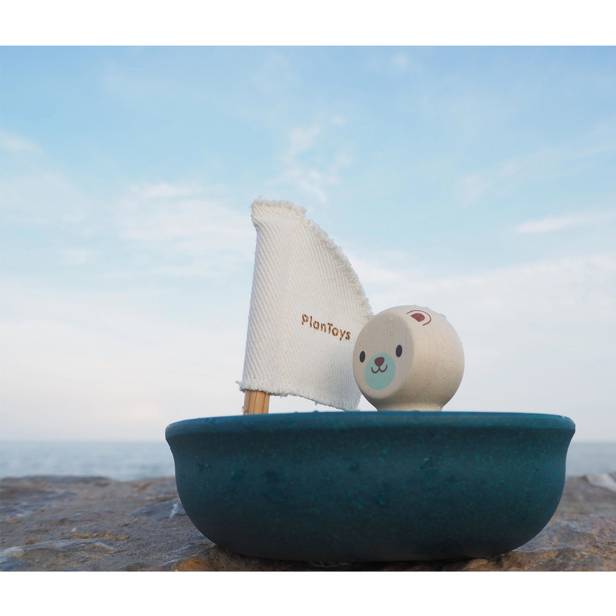 Wooden toy sailboat with a white sail and a small character figure on a blue background.
