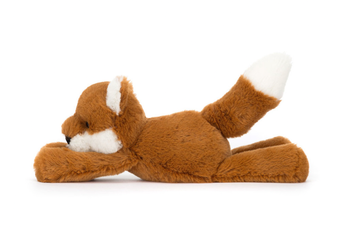 A plush toy representing a dark orange fox with fluffy cream ears and a tail, lying down on a plain background.