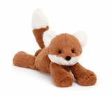 A plush toy representing a dark orange fox with fluffy cream ears and a tail, lying down on a plain background.