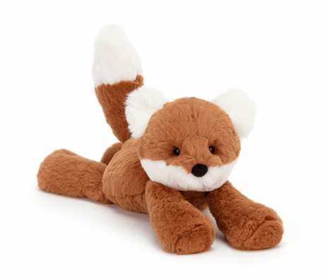 A plush toy representing a dark orange fox with fluffy cream ears and a tail, lying down on a plain background.