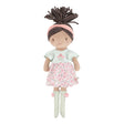 Soft doll with floral pink and sage green dress, pink headband and sage green socks with pink pompoms. Curly brown hair tied in a ponytail.