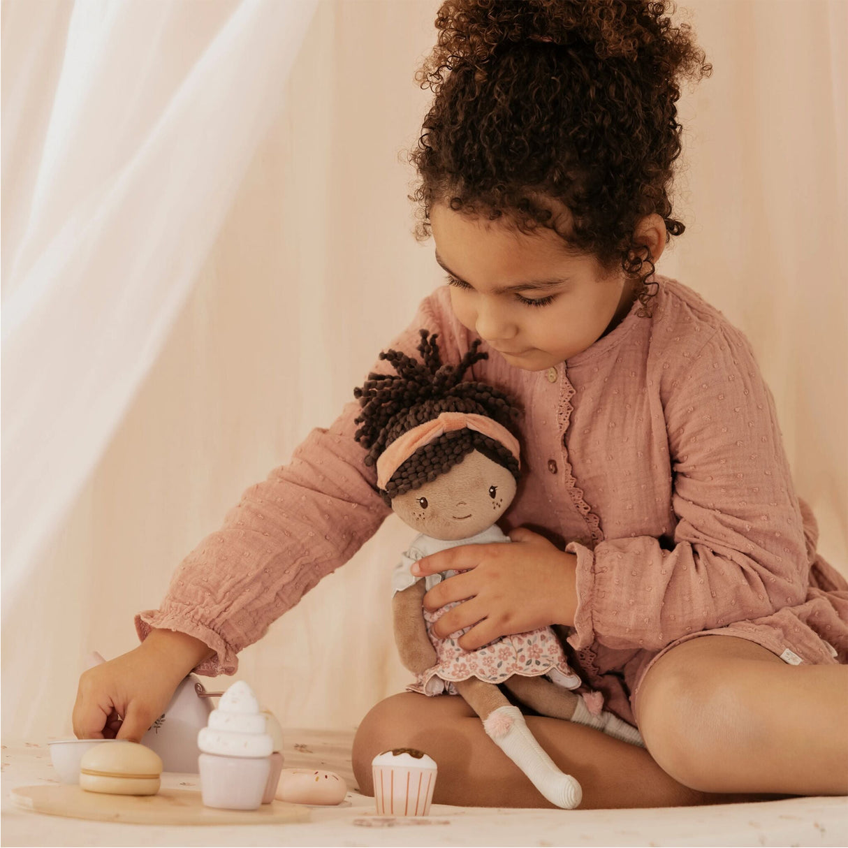 Little girl playing tea party with a soft doll in a floral pink and sage green dress