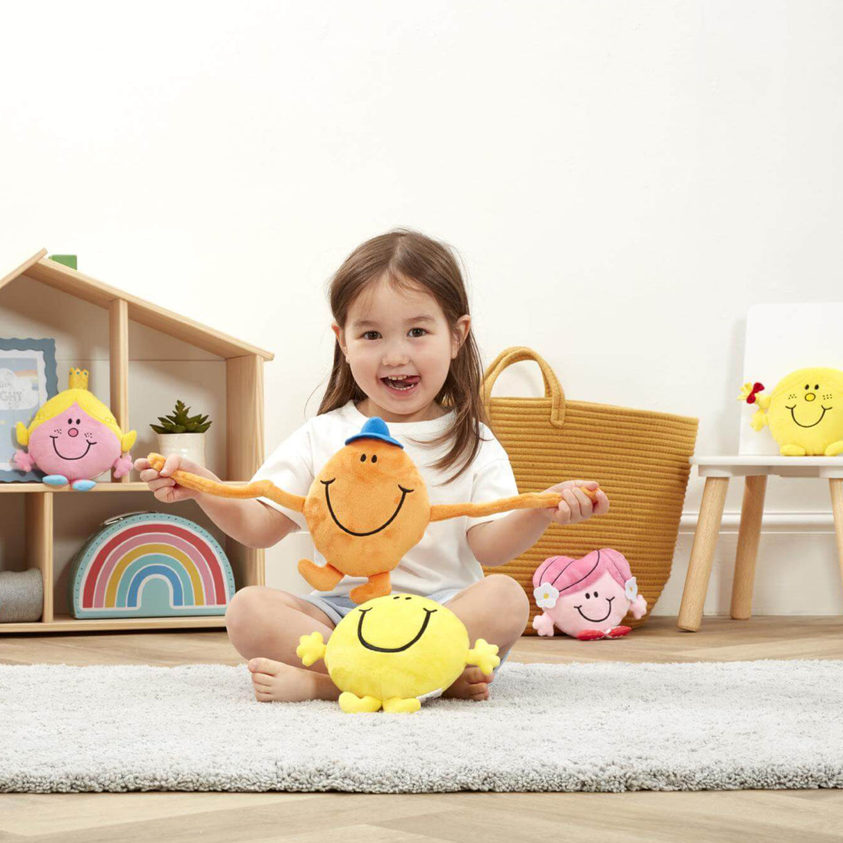 Child sitting holding Mr tickle surrounded by mr men and little miss soft toys