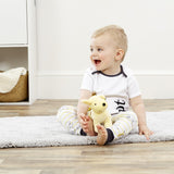 Baby sitting on a rug holding a yellow plush Spot the Dog soft toy in a room with white walls and wooden floor.