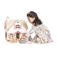 Young girl playing with a wooden dollhouse and accessories on a white background