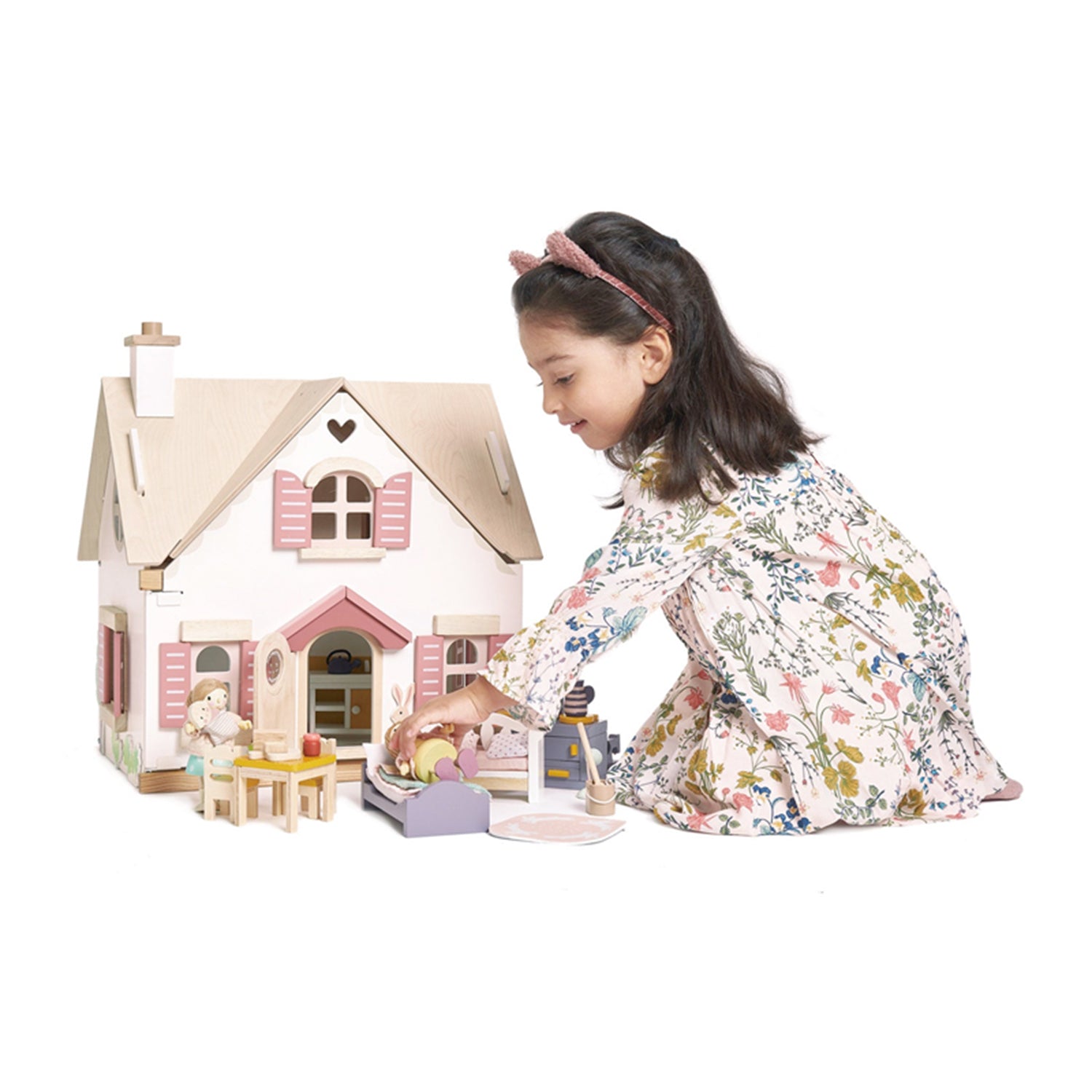 Young girl playing with a wooden dollhouse and accessories on a white background