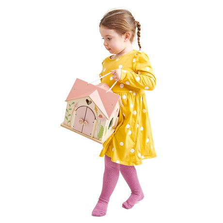 Child in a yellow dress holding a pink flower painted toy house on a white background
