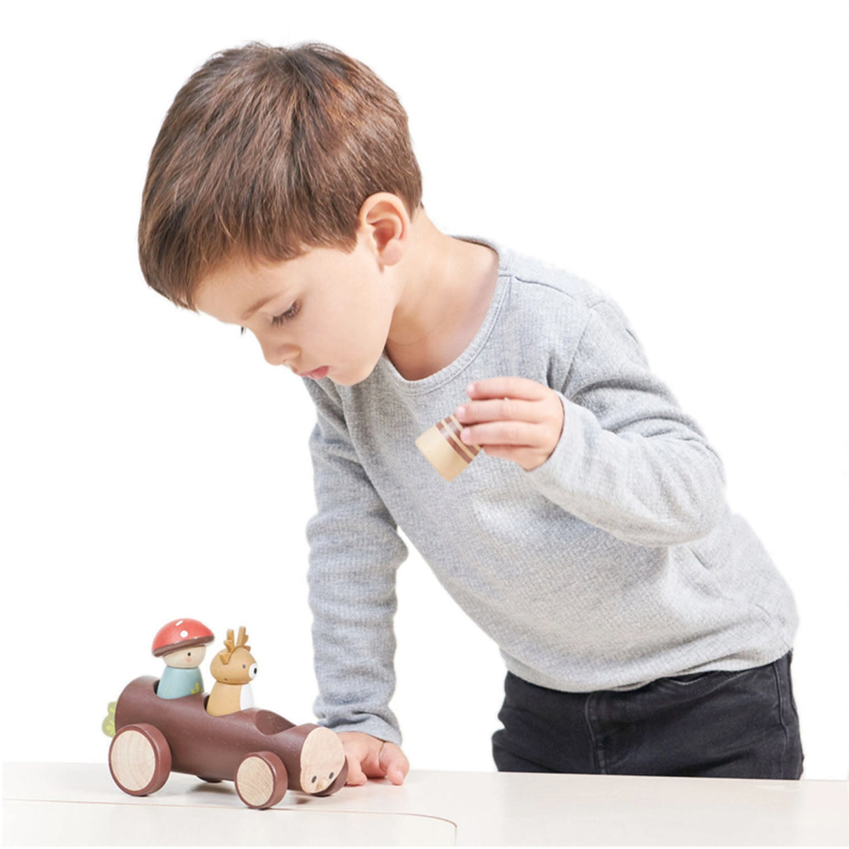 Child playing with a wooden toy car on a white background
