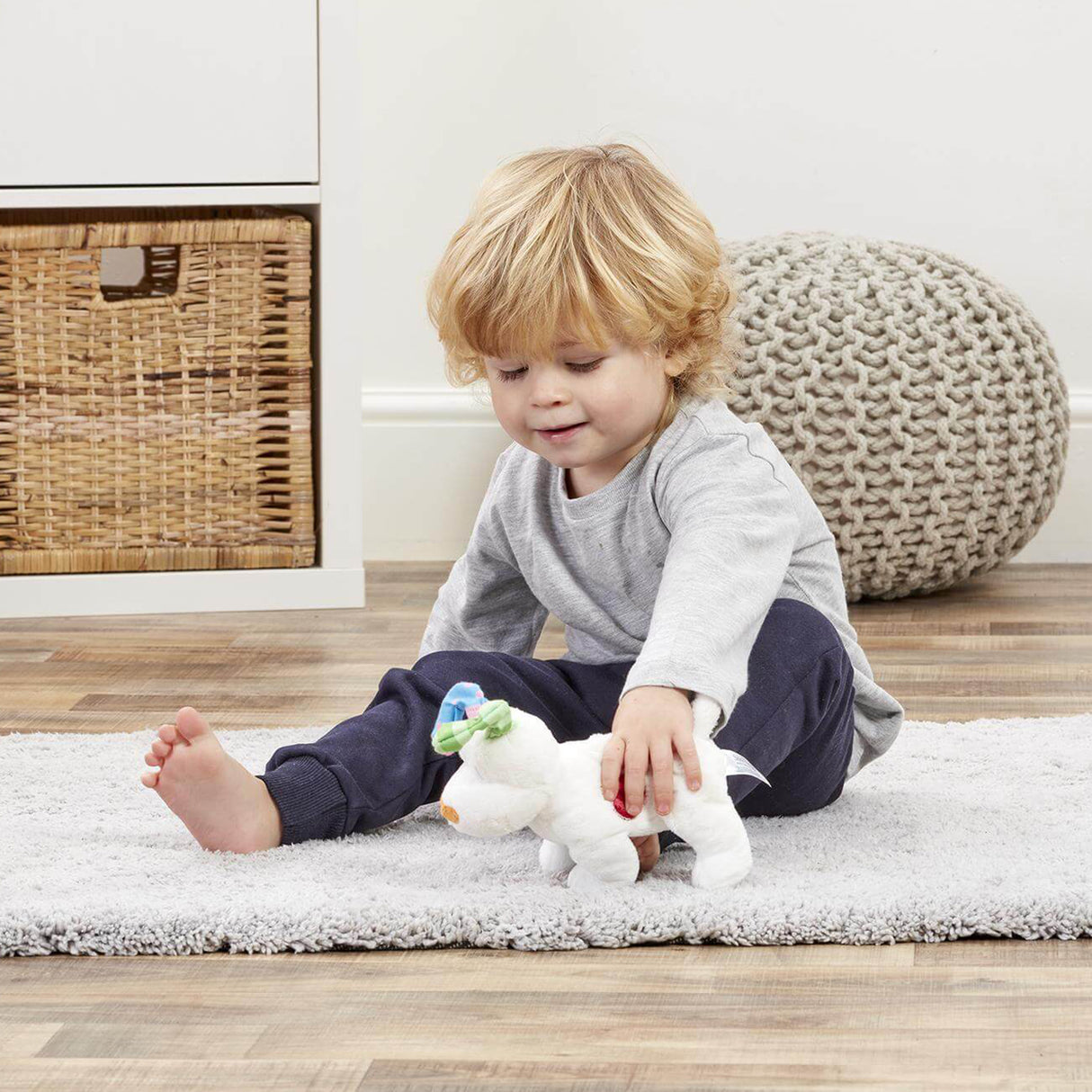 Child sitting on a rug holding a plush Snowfdog toy in a room with a wicker basket and textured chair.