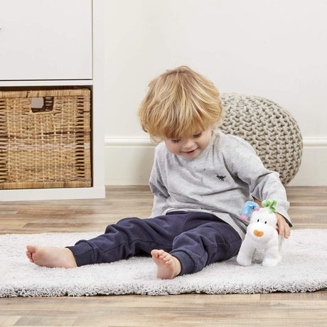 Child sitting on a rug holding a plush Snowfdog toy in a room with a wicker basket and textured chair.