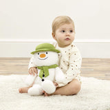 Baby holding a plush snowman toy on a light-colored rug.