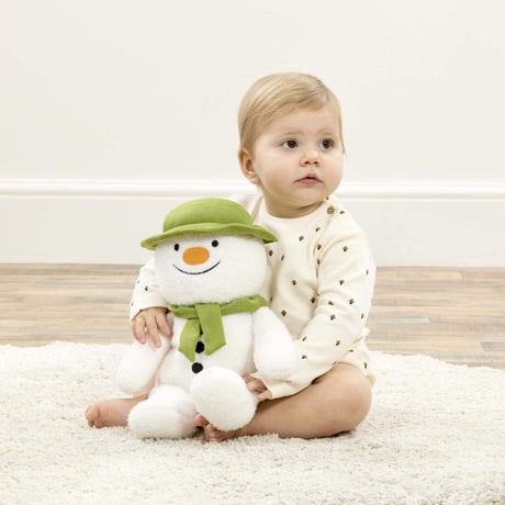 Baby holding a plush snowman toy on a light-colored rug.