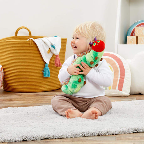 Child holding a soft caterpillar toy in a room with a basket and colourful decor