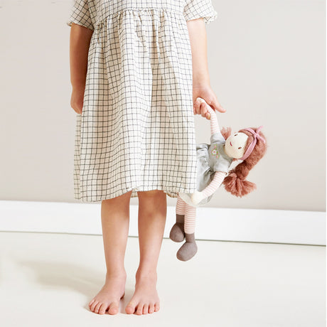 Child wearing a checkered dress holding a rag doll on a white background