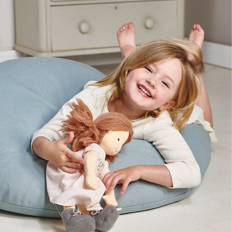 Child sitting on a blue cushion holding a doll in a room with white furniture.