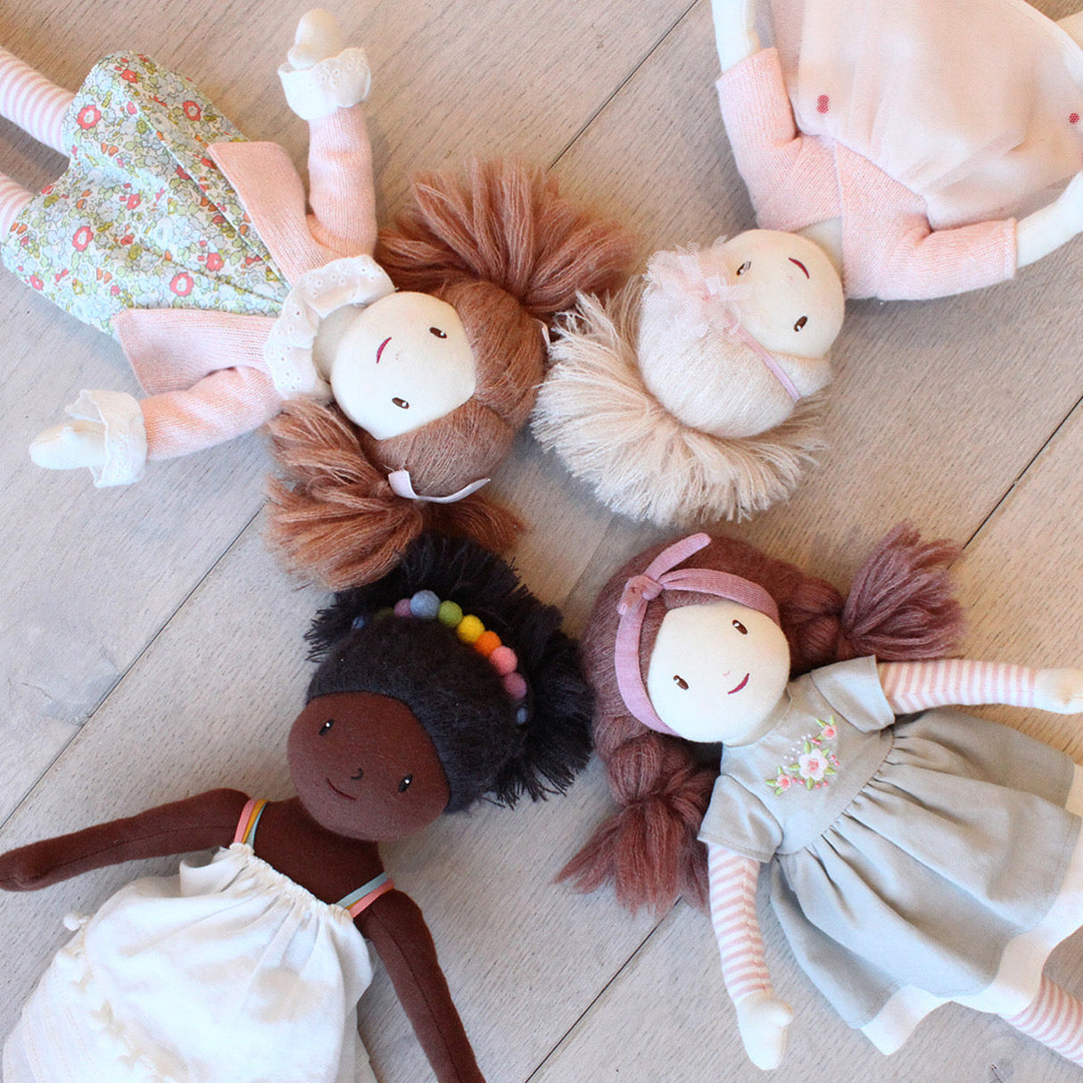 Set of soft dolls with different hair colours and outfits on a wooden floor.
