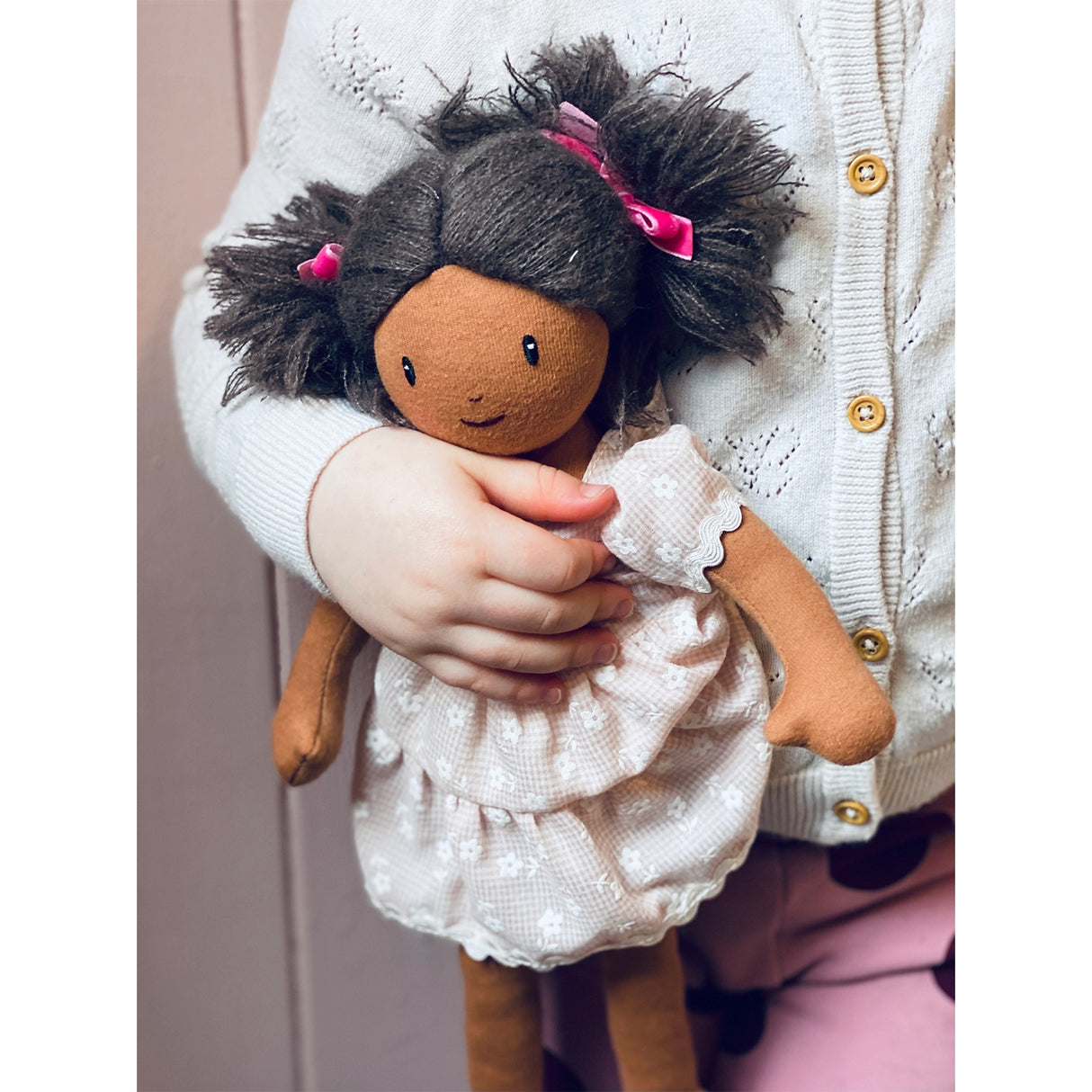 Child holding a plush doll with dark hair and a white outfit.