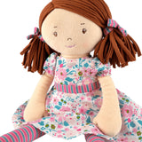 Soft rag doll with brown hair with pigtails wearing a floral pink and turquoise dress, stripey tights sitting
